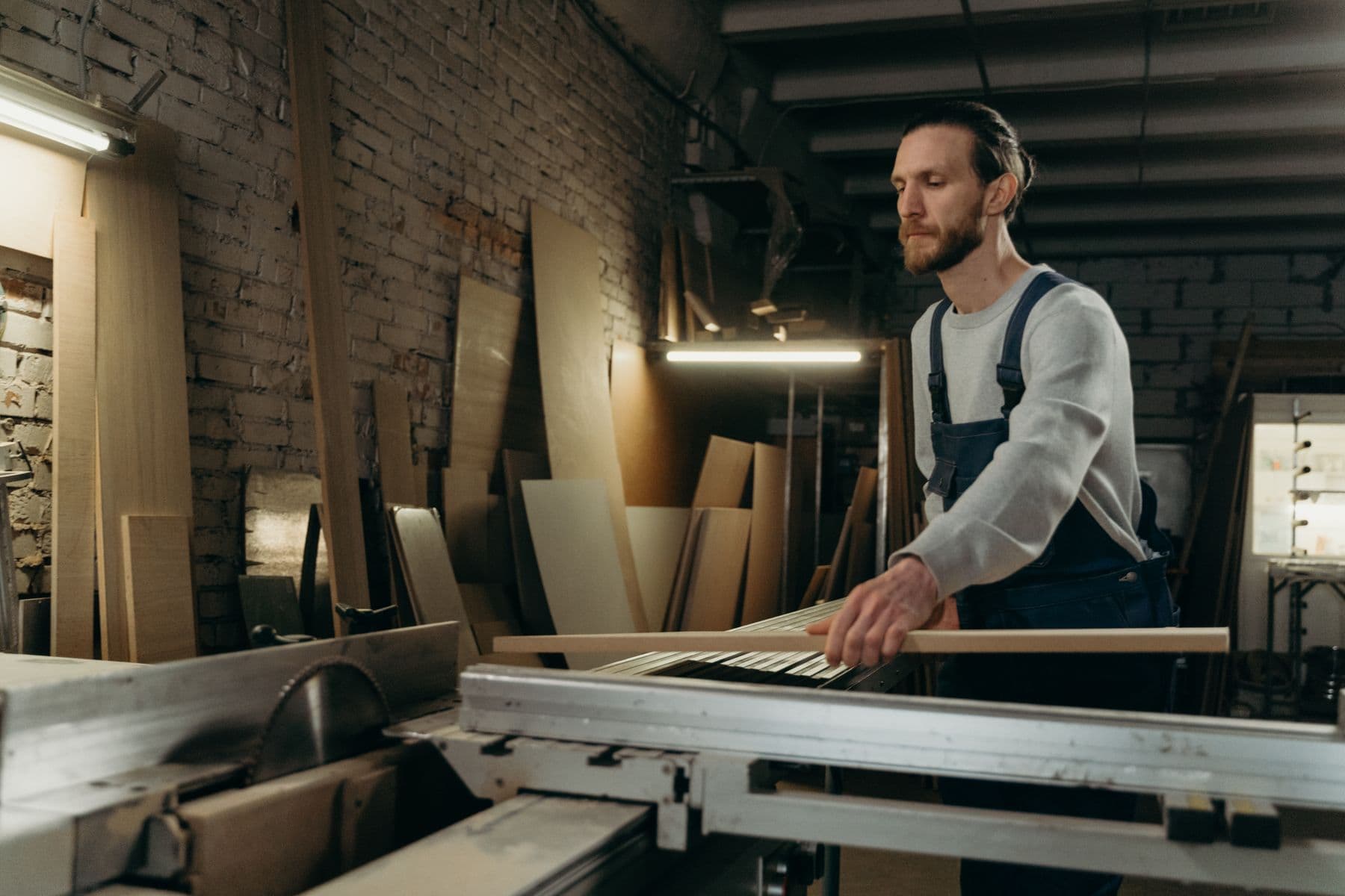 A craftsman in an apron working at a bench in a brick-walled woodworking workshop