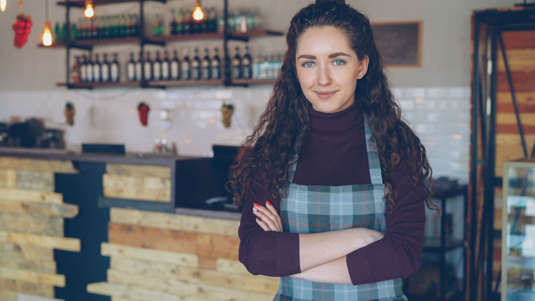 The owner of a neighborhood café standing behind her counter with her arms crossed, smiling at the camera