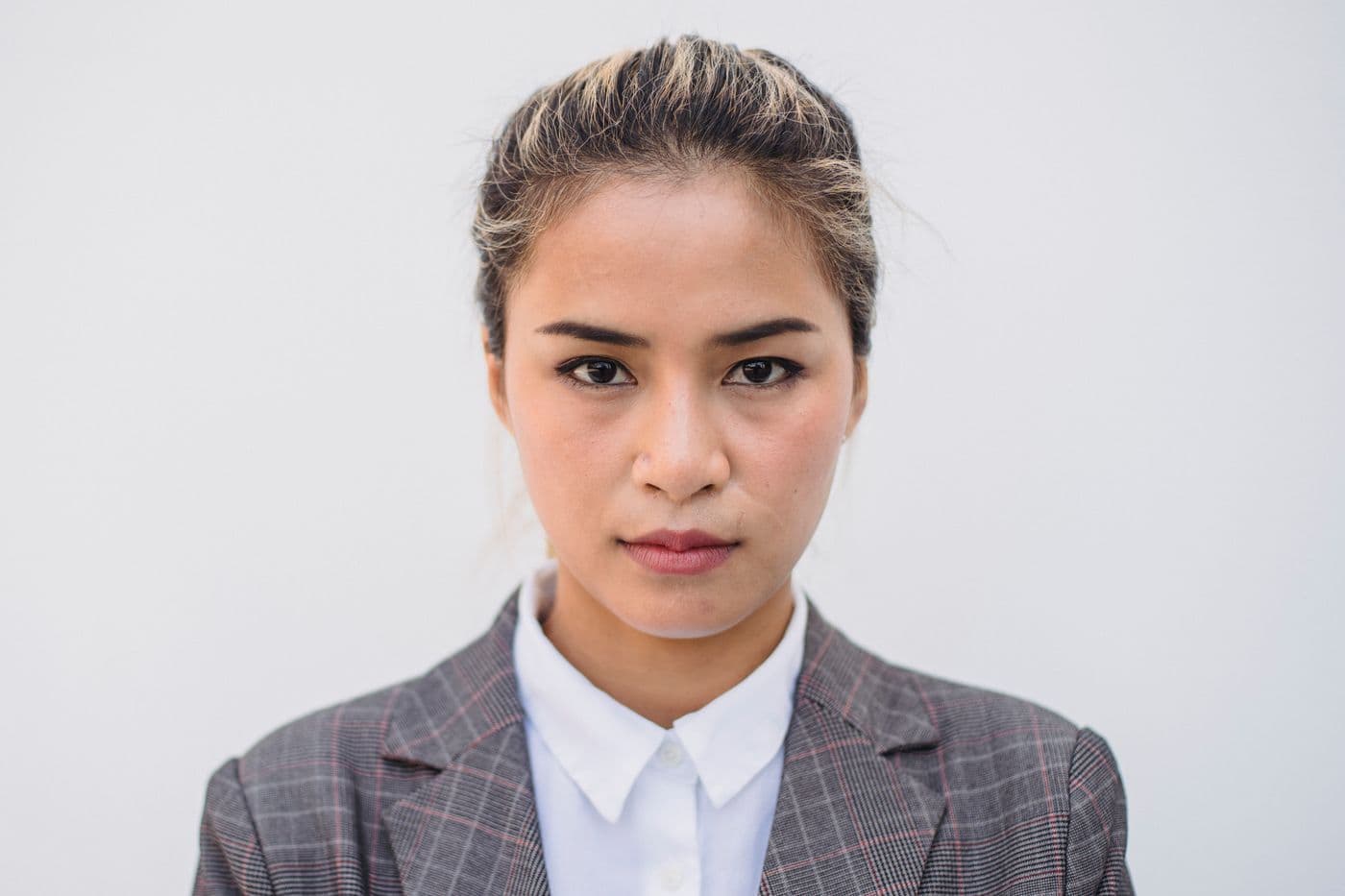 Portrait of Mei Tanaka against a light grey wall, wearing a grey blazer